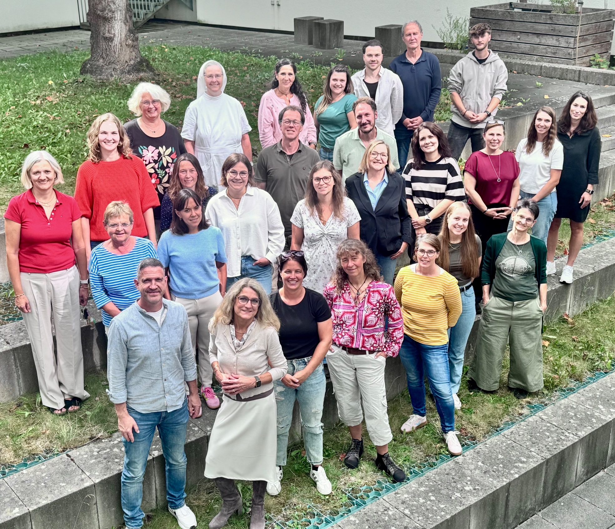 Gruppenfoto von mehreren Personen in einem Garten, unterschiedliche Kleidung und Posen.