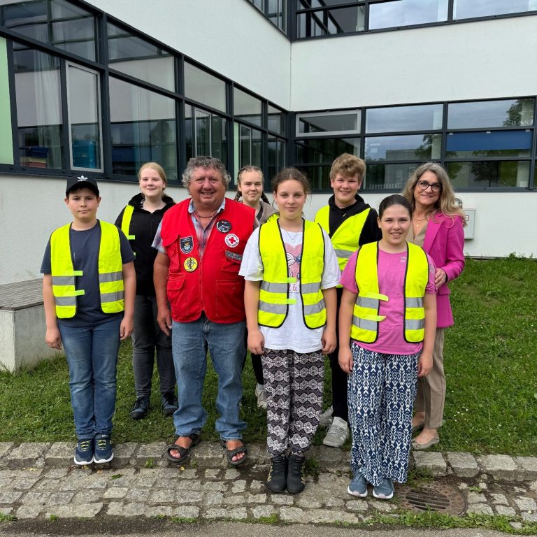 Schulsanitätsdienst Gruppenfoto von Kindern und Erwachsenen in gelben Warnwesten vor einem Gebäude.