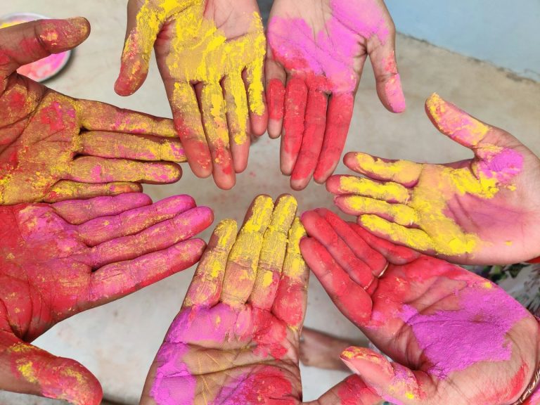OGS Impression Bunte Hände in verschiedenen Hauttönen, mit Pulverfarben in Pink, Gelb und Rot bedeckt.