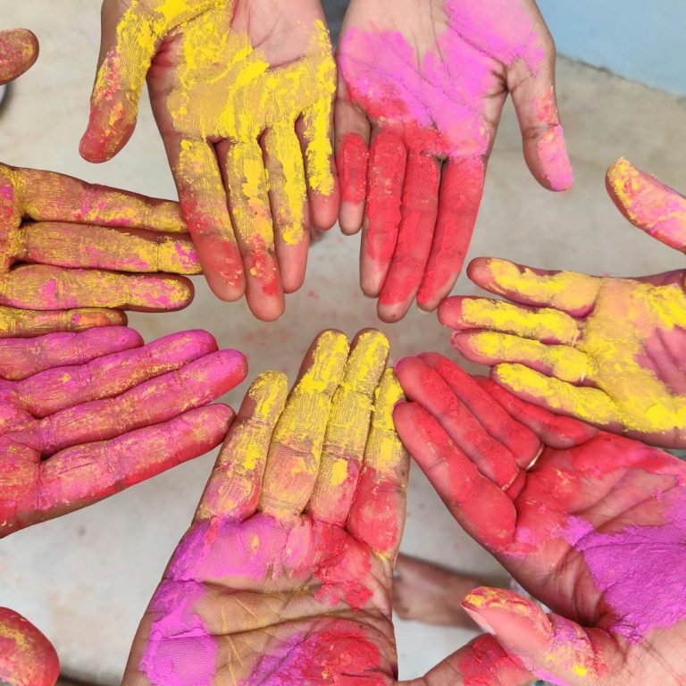 Bunte Hände in Pink, Gelb und Rot liegen kreisförmig zusammen.