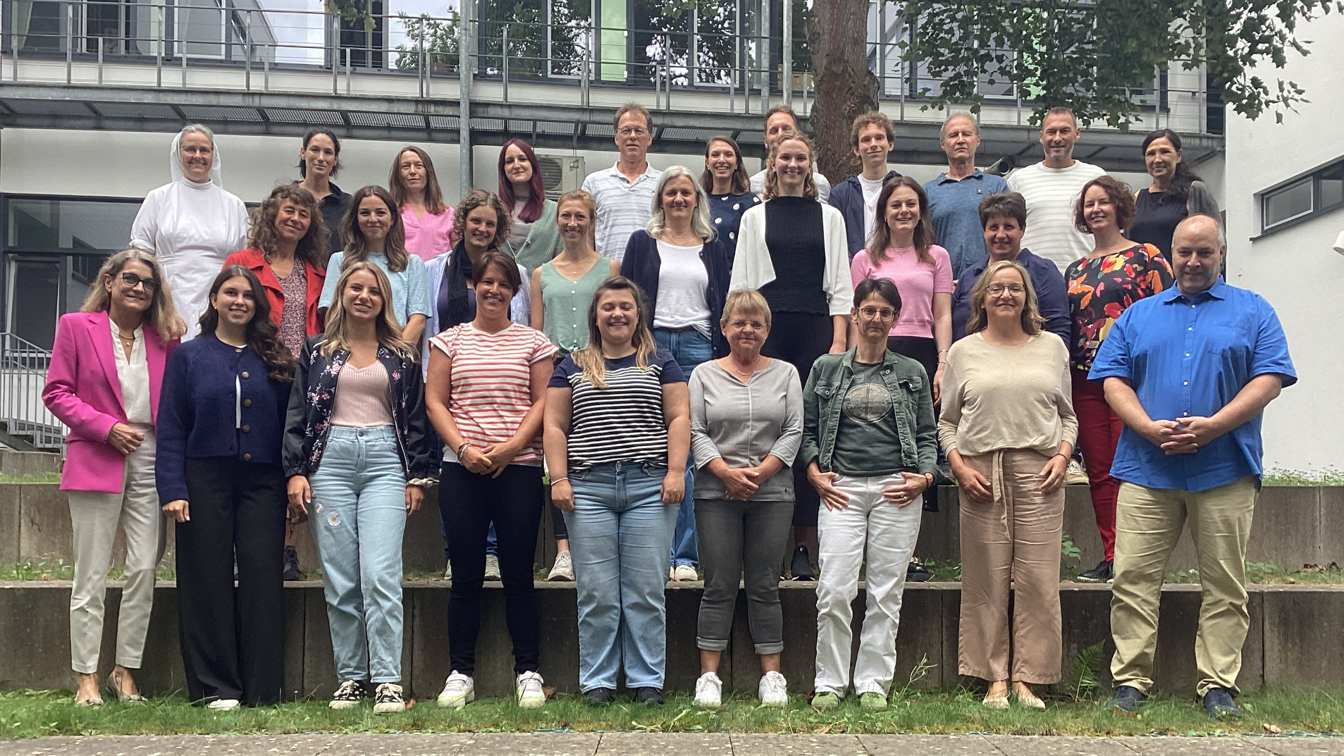 Kollegium der Grund- und Mittelschule Dinkelscherben Gruppenfoto von mehreren Personen in einem Garten, unterschiedliche Kleidung und Posen.