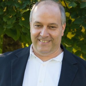 Mann in Sakko lächelt vor grünem Hintergrund.