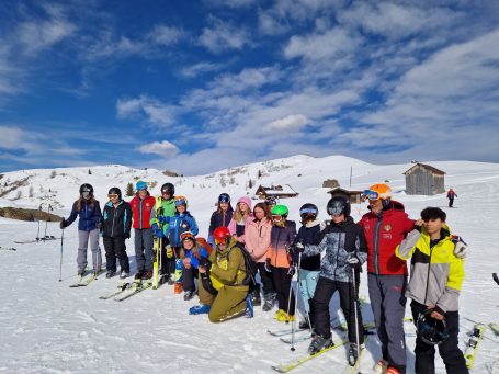 Gruppe von Skifahrern in Winterkleidung auf schneebedecktem Hang mit blauem Himmel.
