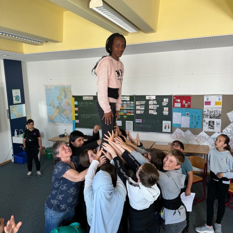 Erasmus+ Gruppenfoto Ein Kind steht auf einem Haufen anderer Kinder, die sie von unten stützen.