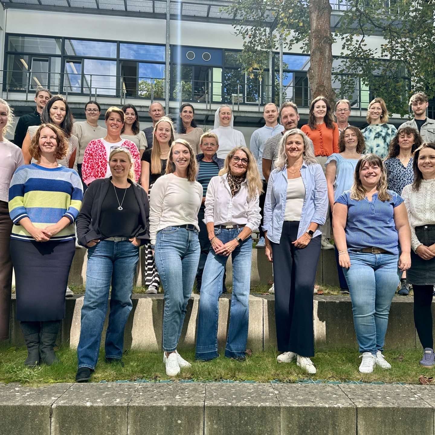 Kollegium der Grund- und Mittelschule Dinkelscherben Gruppenfoto von mehreren Personen in einem Garten, unterschiedliche Kleidung und Posen.